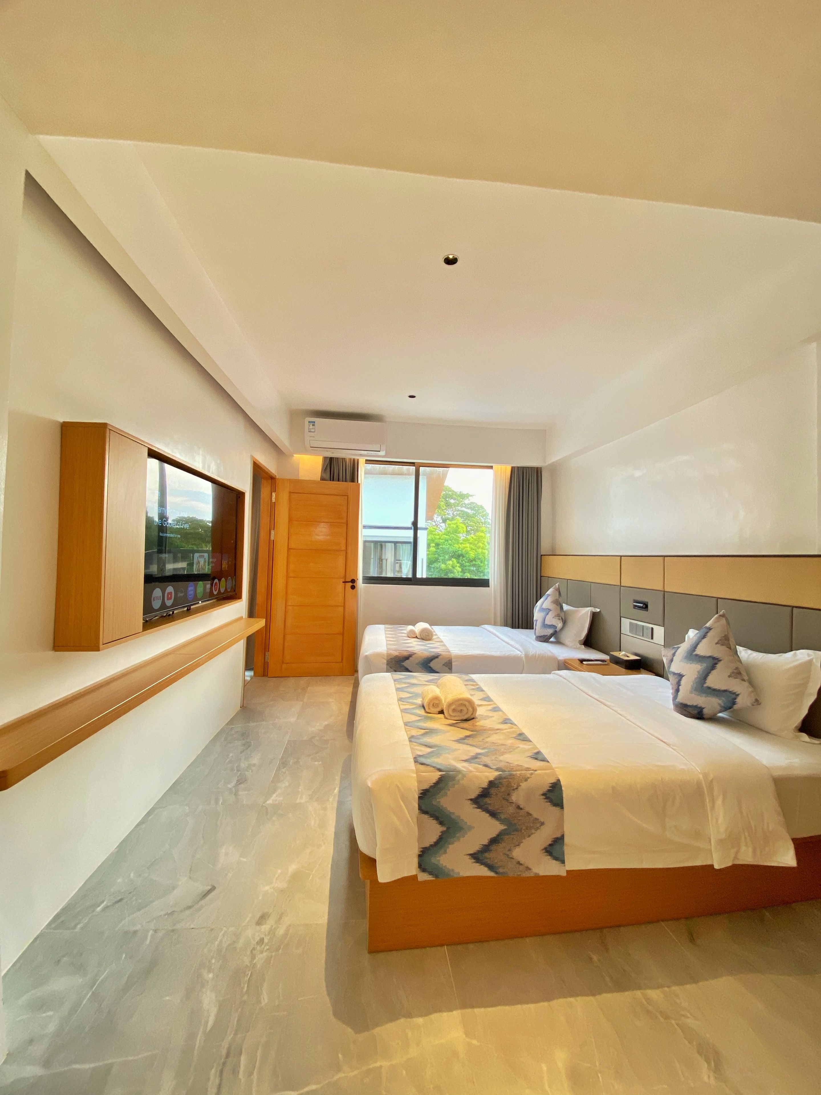 Habitación de hotel moderna con una cama grande, un televisor montado en la pared y una ventana con cortinas.