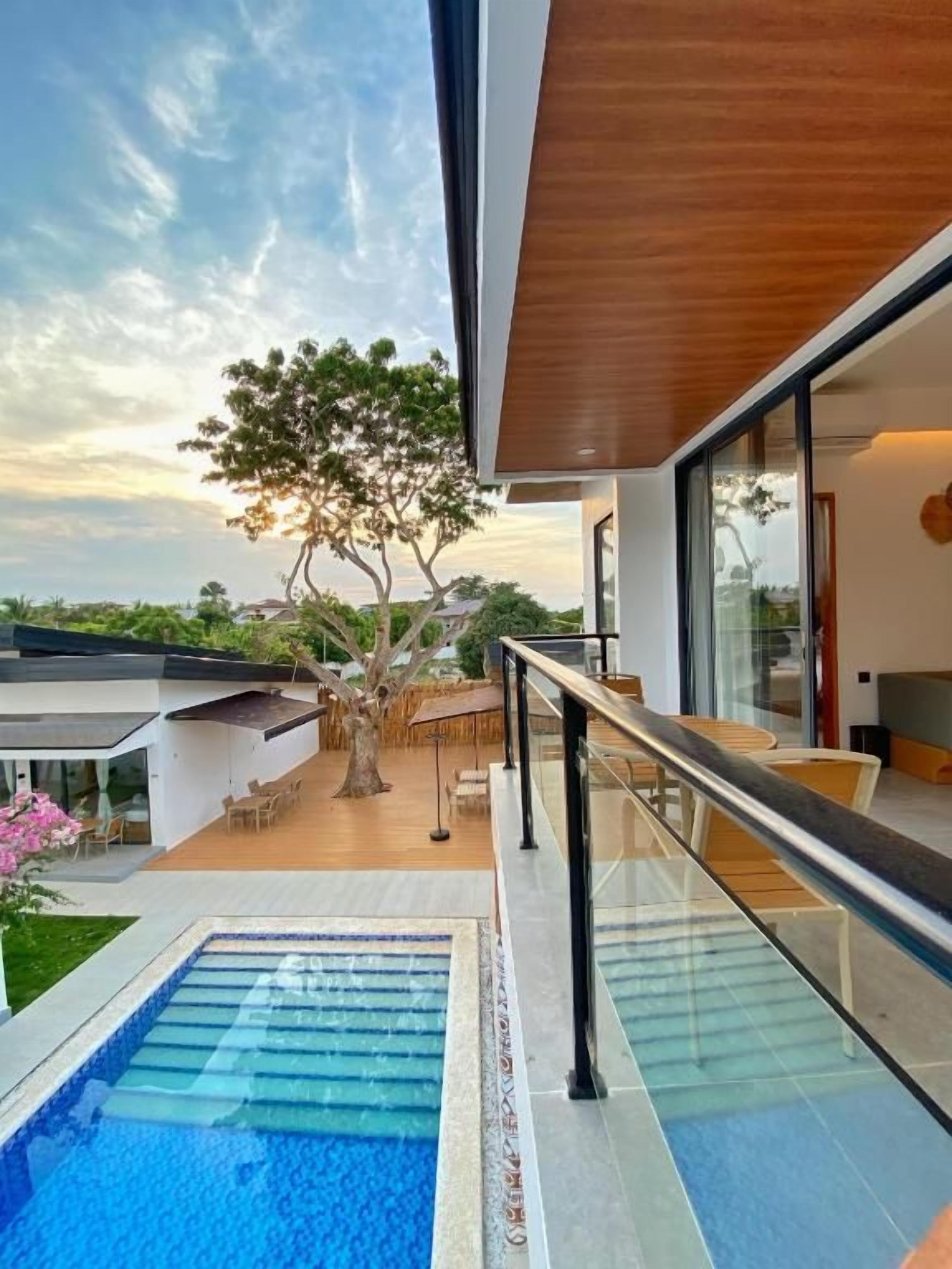 Un área de piscina moderna al aire libre con barandilla de cristal, terraza de madera y vistas del paisaje circundante.