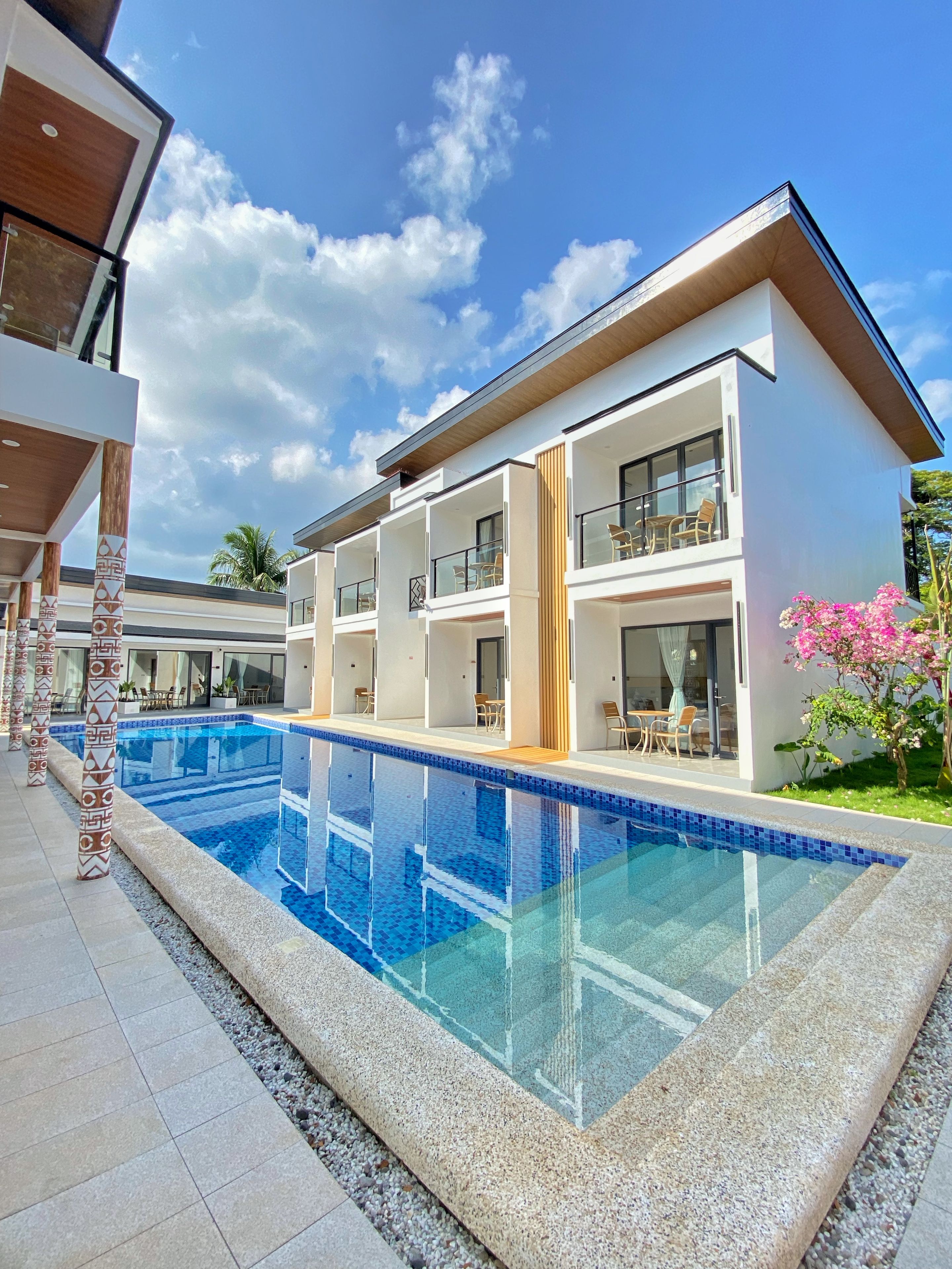 Un hotel moderno de varios pisos con piscina, asientos al aire libre y un cielo azul despejado.