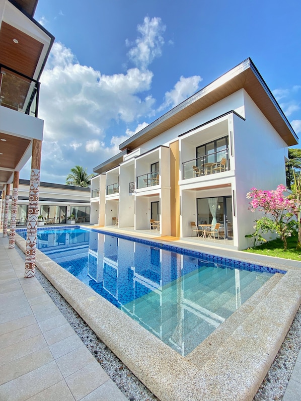 A modern multi-story hotel with a swimming pool, outdoor seating, and a clear blue sky. - diver's home resort (Panglao)