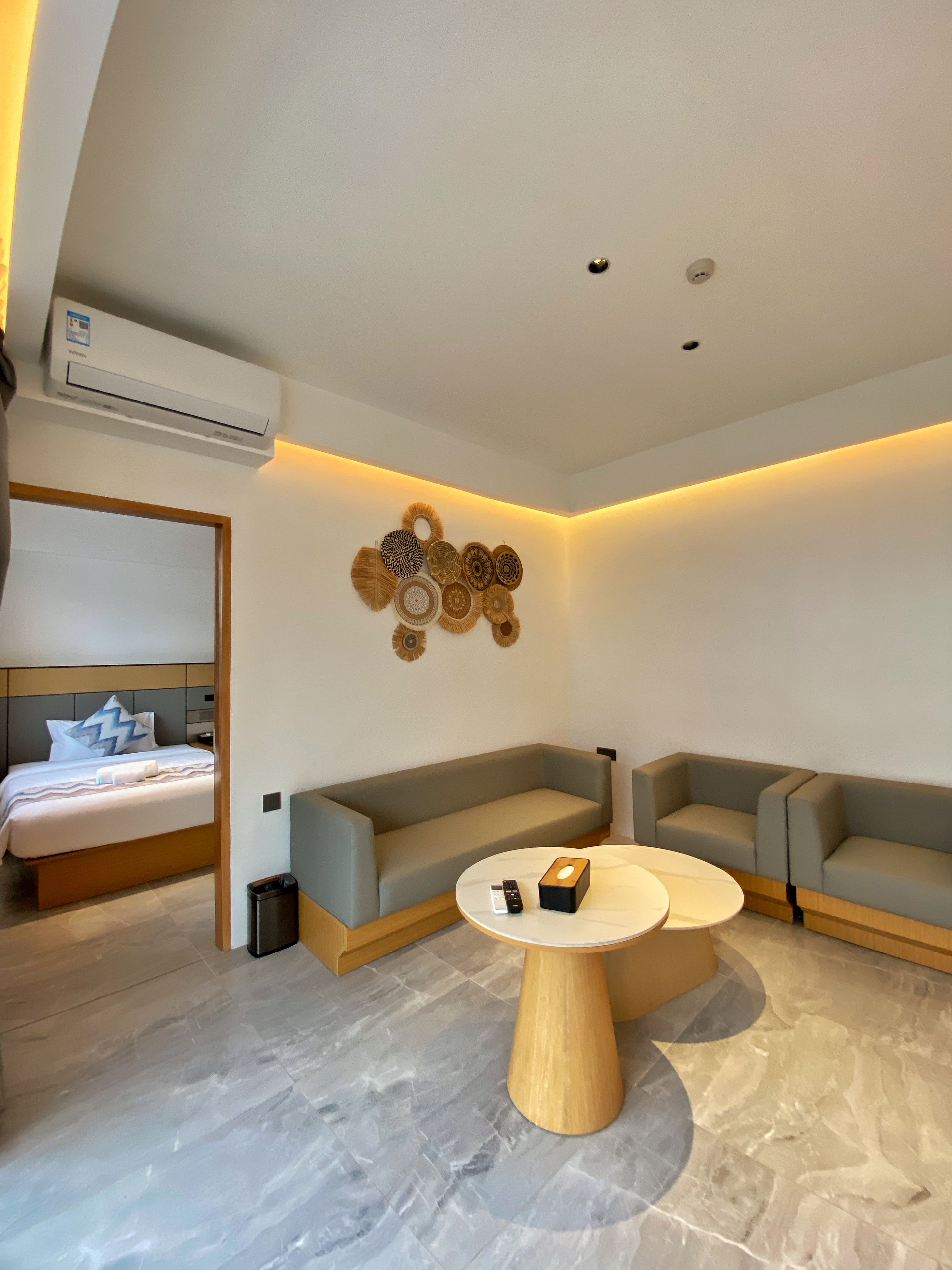 Een moderne hotelkamer met een bed, twee sofa's, een ronde salontafel en een decoratief kunstwerk aan de wand.