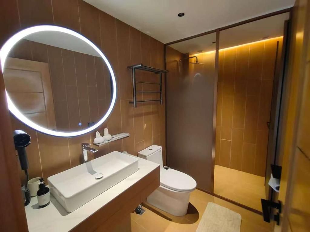A modern bathroom with a round mirror, a white sink, a toilet, and a shower area.