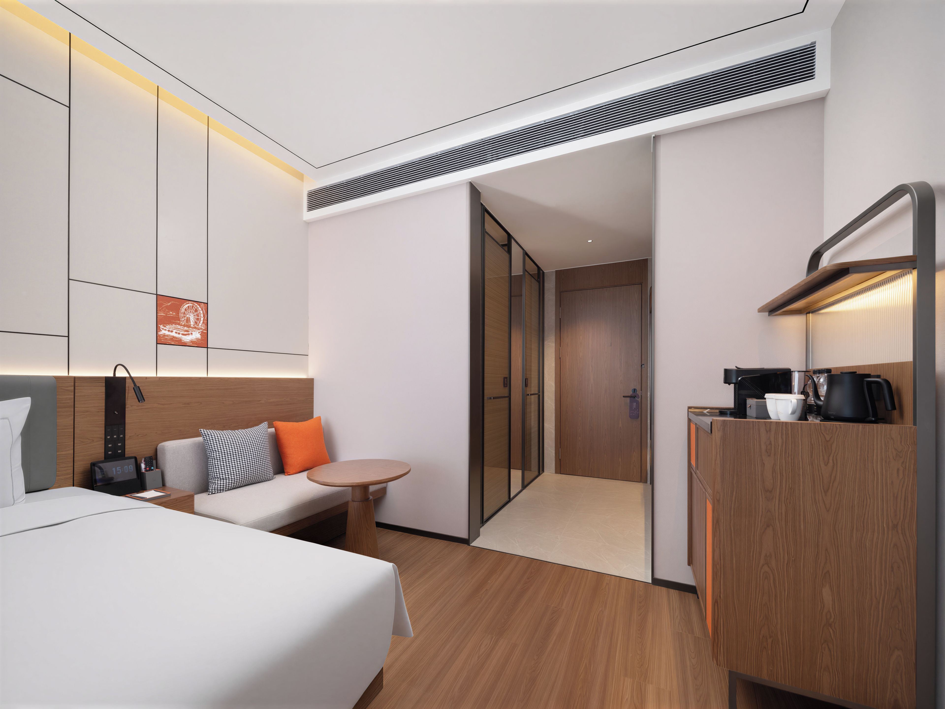 A modern hotel room with a bed, a desk, a coffee maker, and a door leading to a bathroom.
