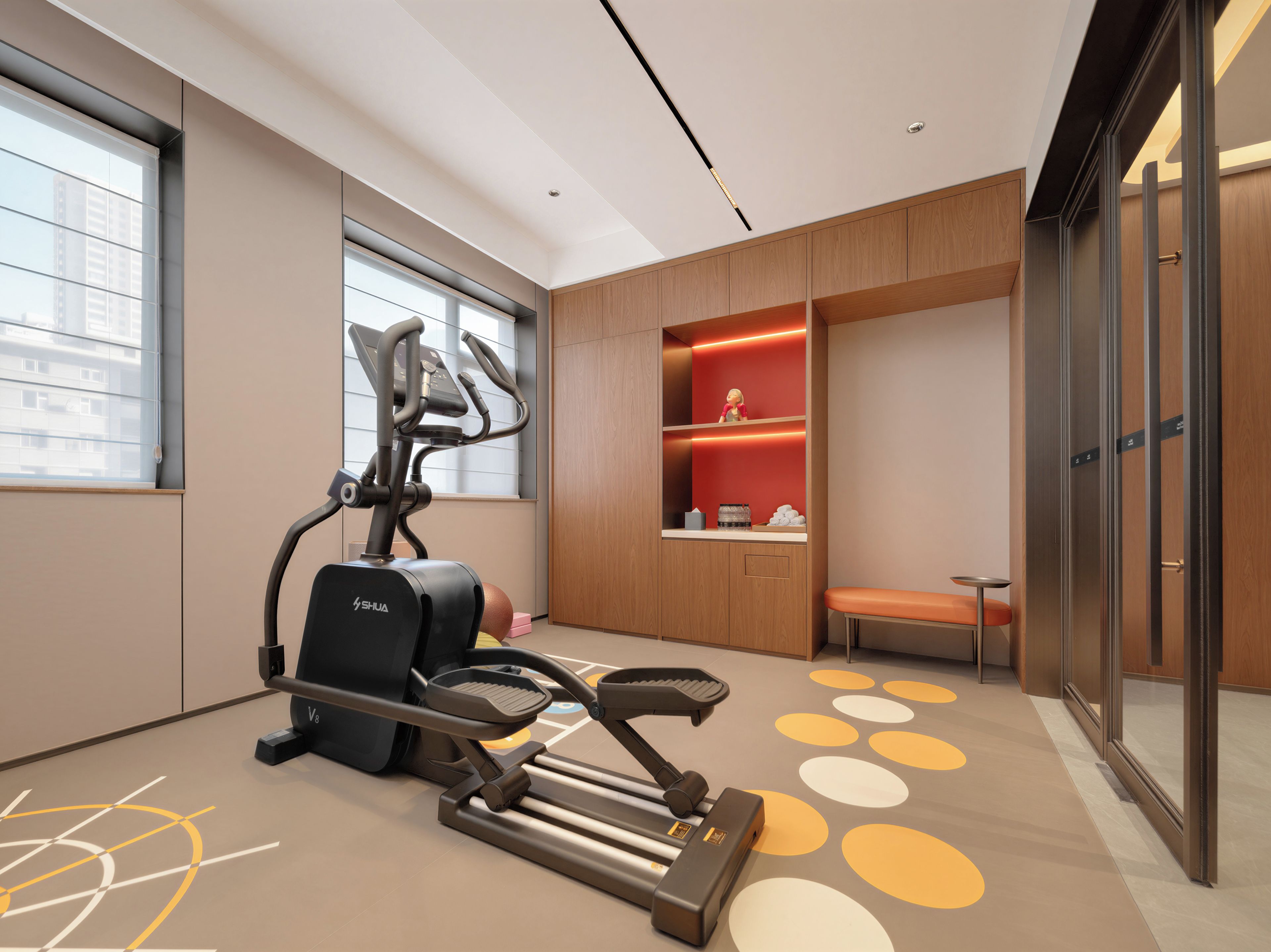 Une salle de sport moderne équipée de matériel d’exercice, dotée d’un espace détente et offrant une vue sur la ville grâce à de grandes fenêtres.
