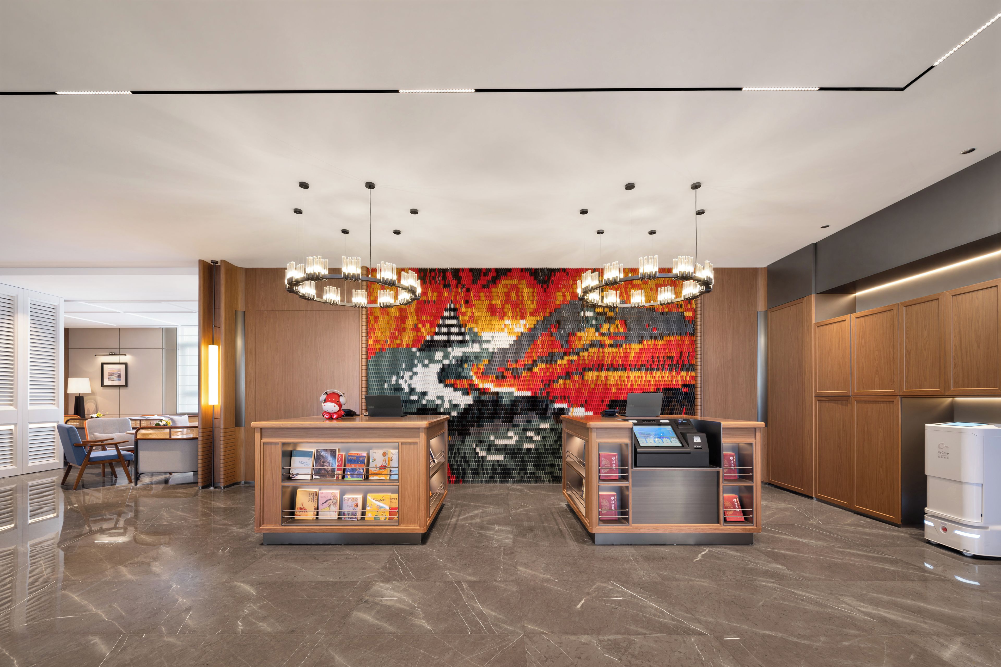 Un área de recepción con diseño moderno, que incluye un quiosco de registro digital, un espacio de descanso con una lámpara e impactante obra de arte mural de colores.