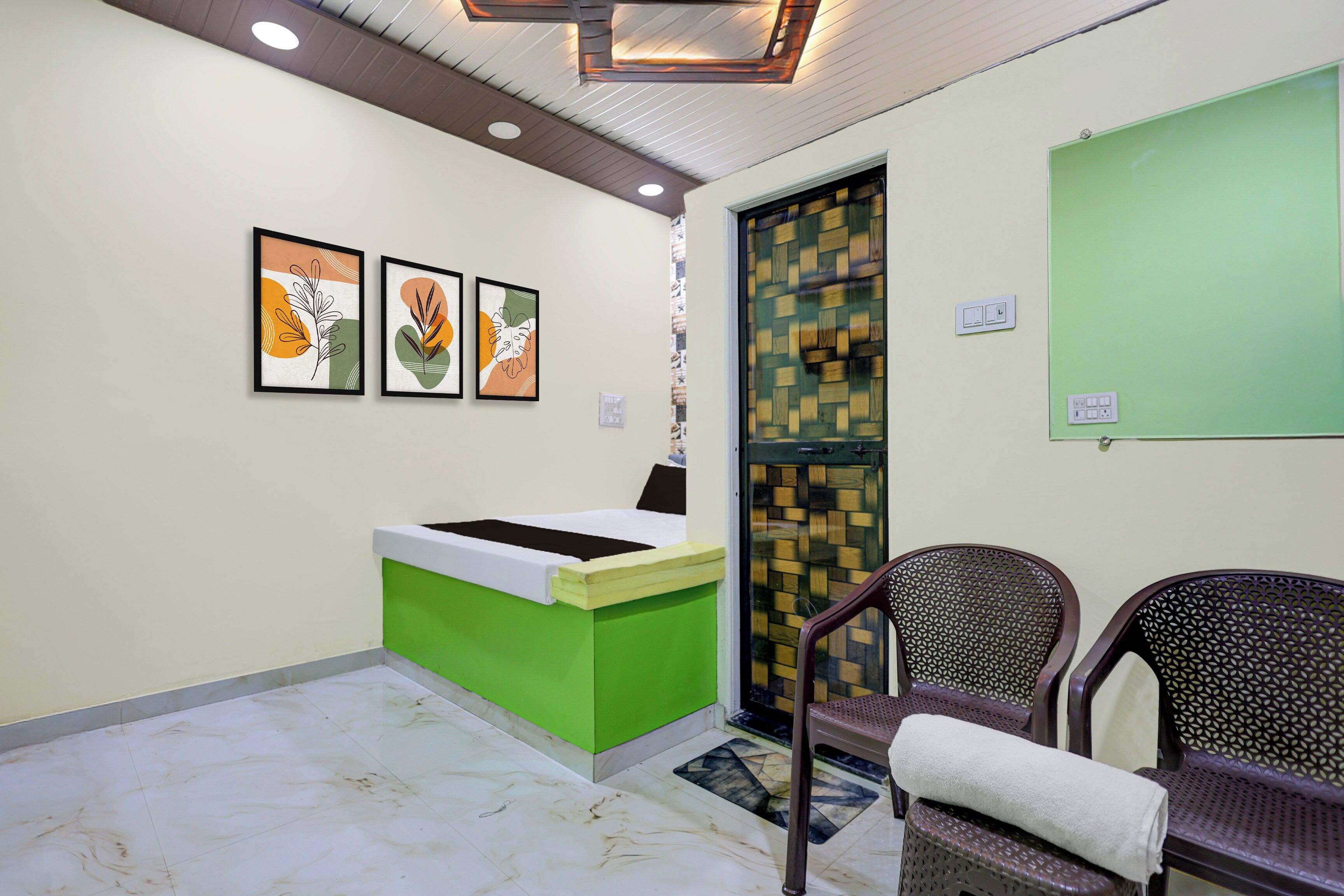 A reception area with a green desk, three framed artworks, a patterned door, and two wicker chairs.