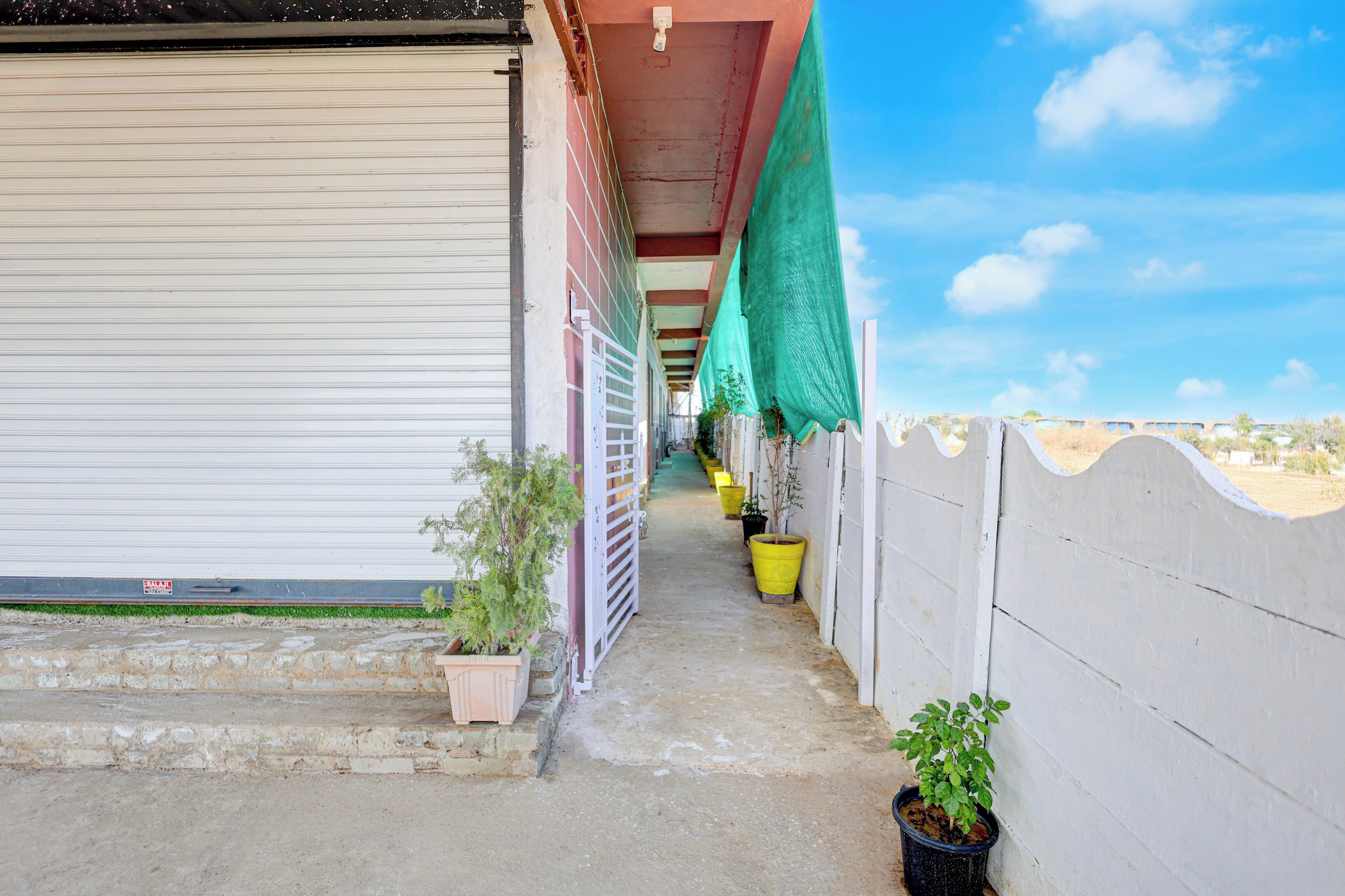 A covered outdoor corridor with potted plants, a closed shutter door, and a clear sky.