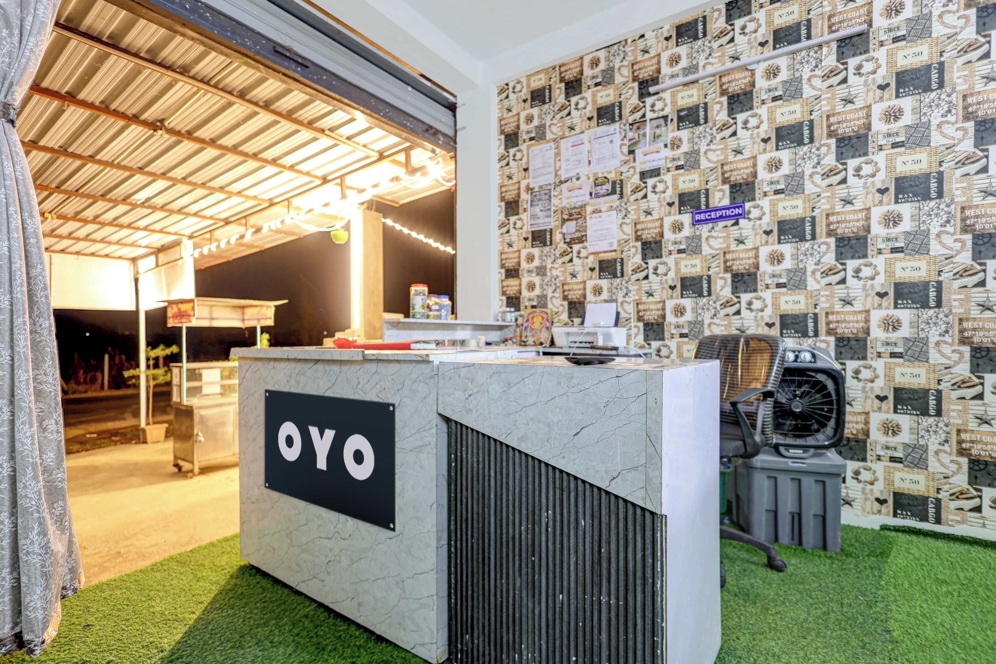 A reception desk with a sign reading 'OYO' in a modern interior with a patterned wall and artificial grass flooring.