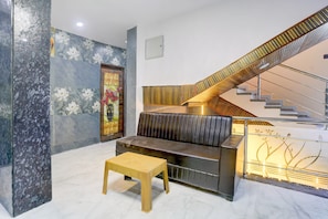 A modern interior with a sofa, a small table, a staircase with a wooden handrail, and a wall with a floral pattern. - HOTEL O HAVELI INN (Hingna)