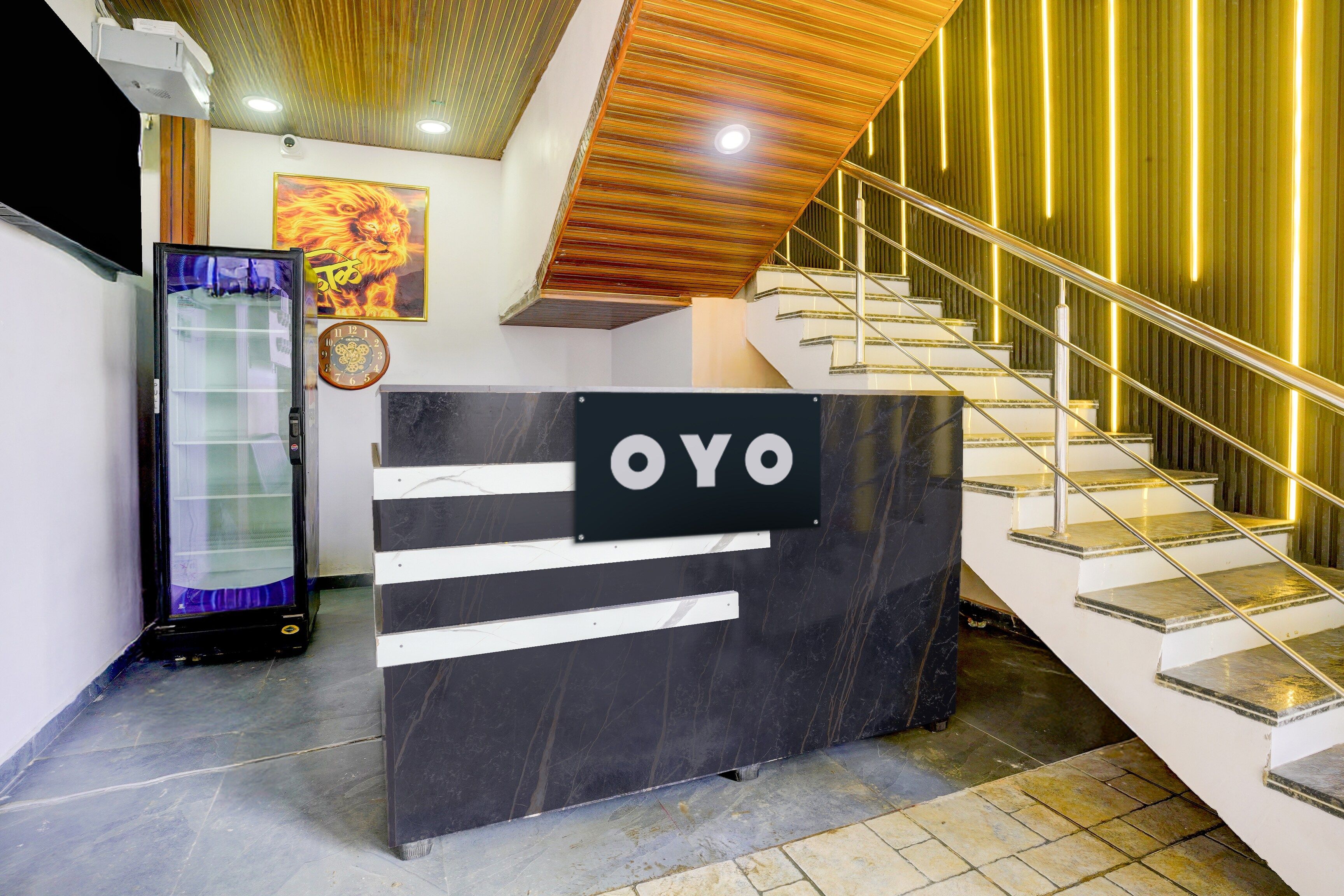 Una recepción con un cartel que dice 'OYO' en un vestíbulo moderno con una escalera y una pared decorativa.