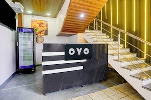 Balcão de recepção com uma placa indicando 'OYO' em um hall moderno com escada e parede decorativa.