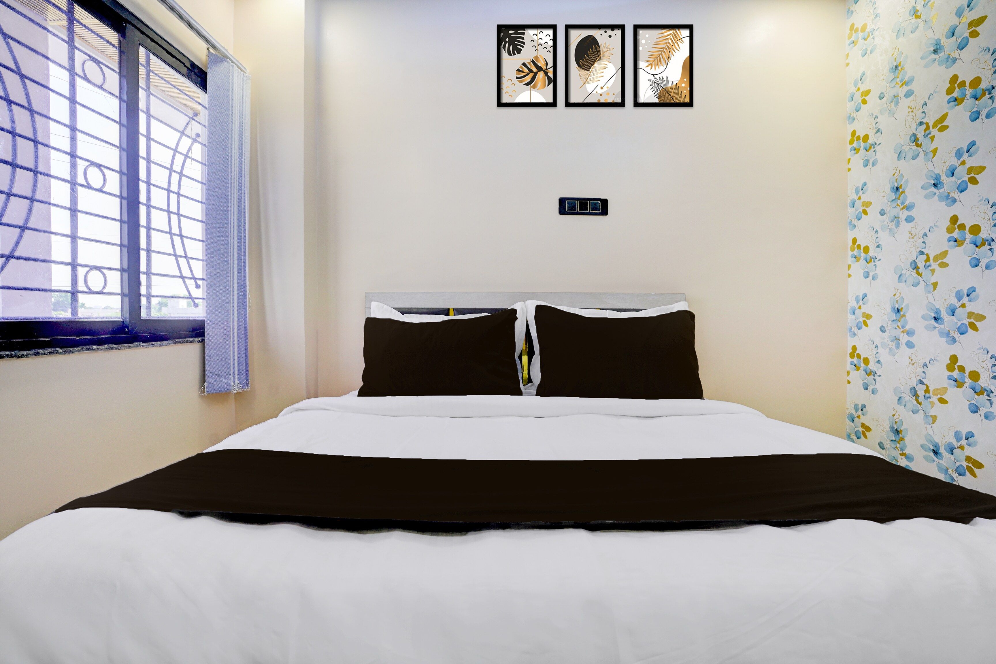 Habitación de hotel con cama, ventana con persianas y pared con tres obras de arte enmarcadas.