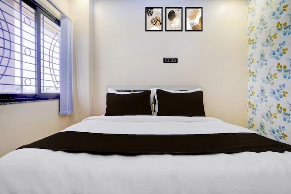 A hotel room with a bed, a window with blinds, and a wall with three framed artworks.