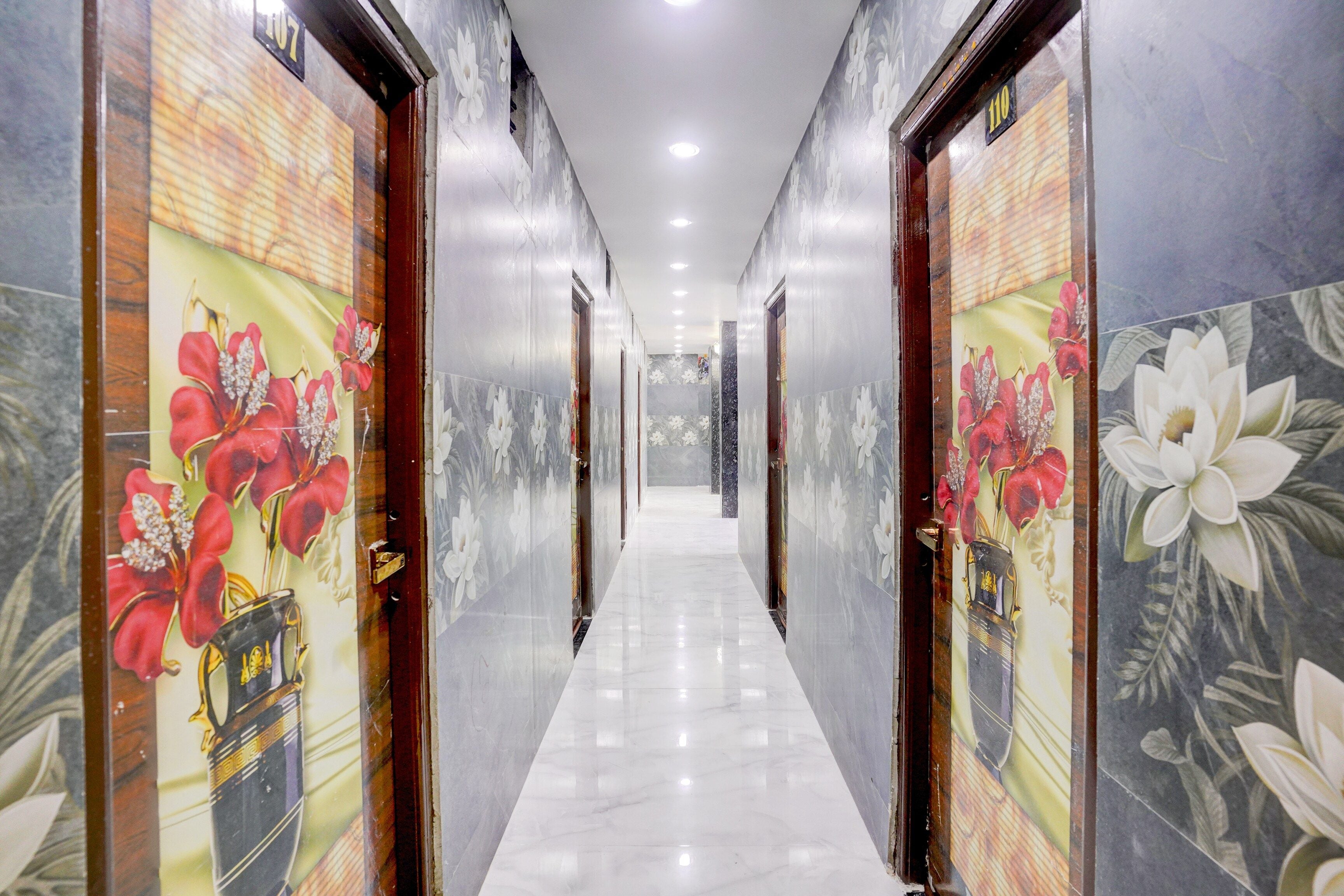 Un pasillo con puertas adornadas con papel tapiz floral, suelo de mármol e iluminación empotrada en el techo.