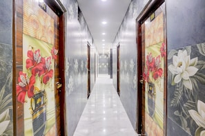 A corridor with doors featuring floral wallpaper, a marble floor, and a ceiling with recessed lighting.