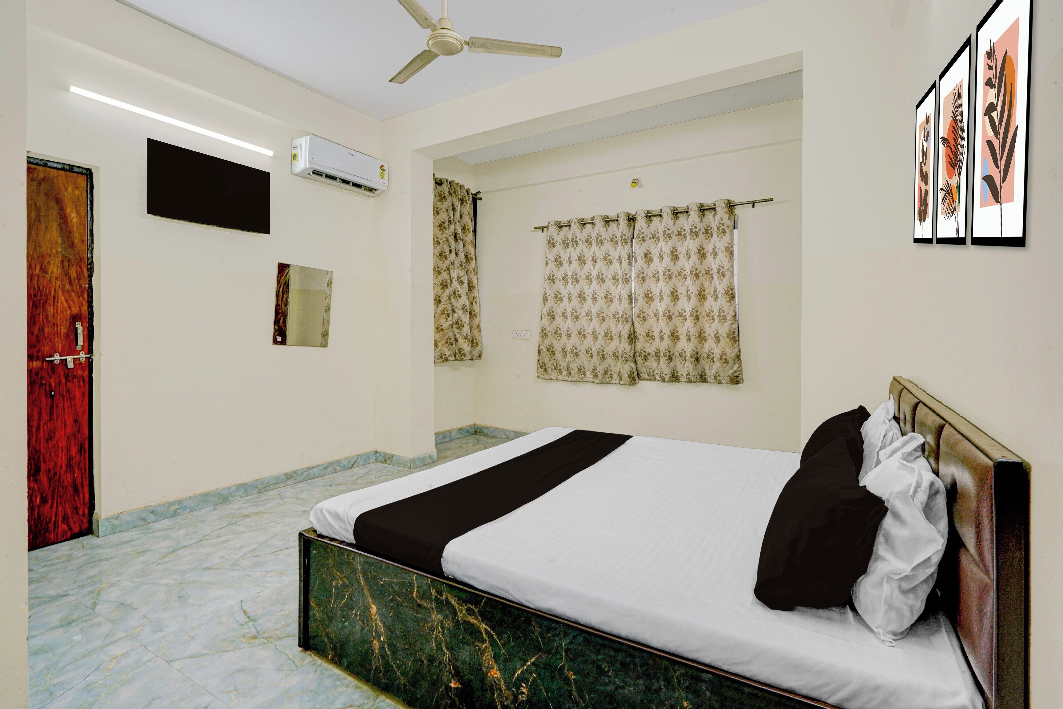 A hotel room with a bed, a ceiling fan, an air conditioning unit, a flat-screen TV, and a window with curtains.