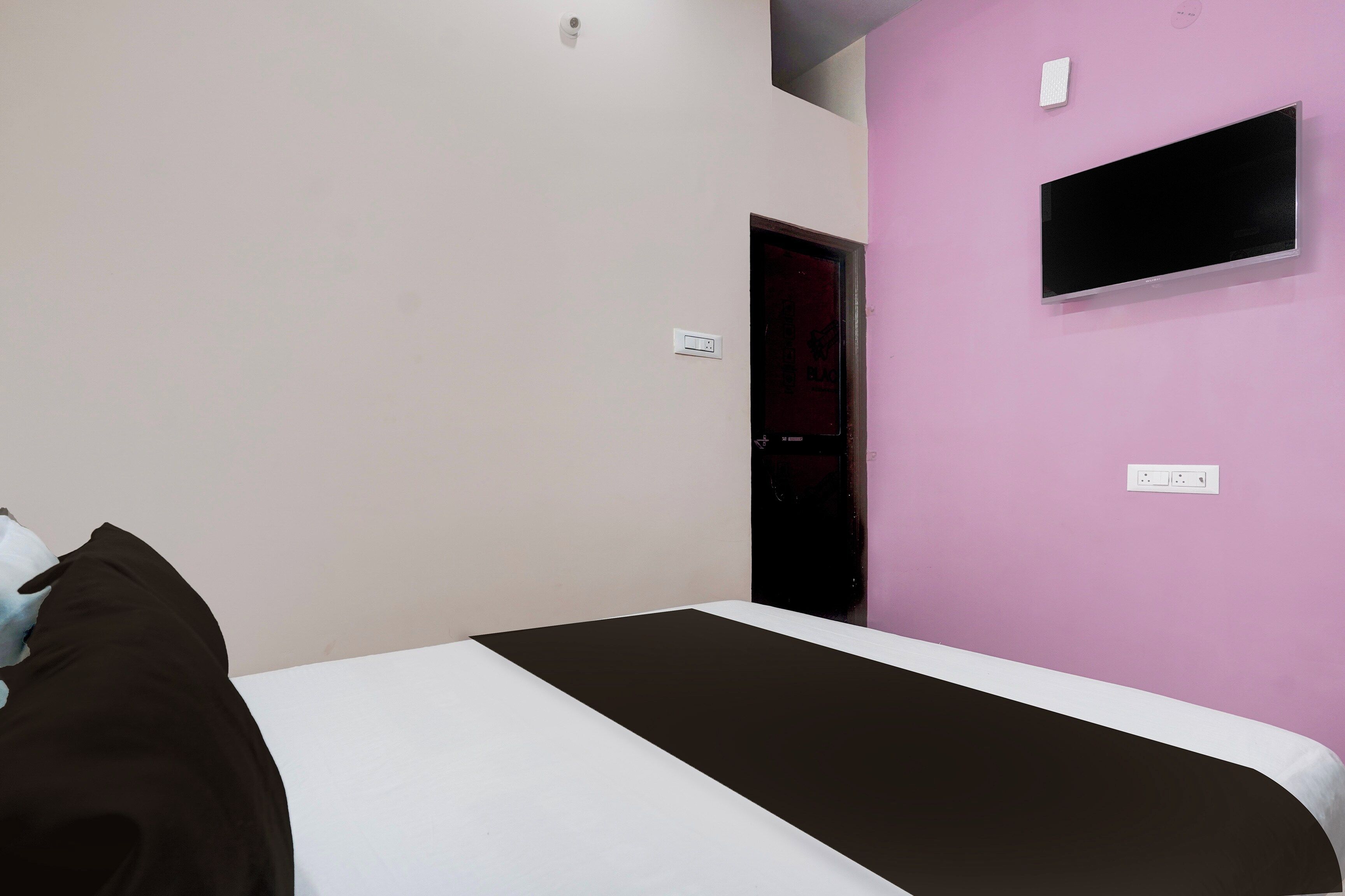 A bedroom with a bed, a television on the wall, and a door leading to another room.