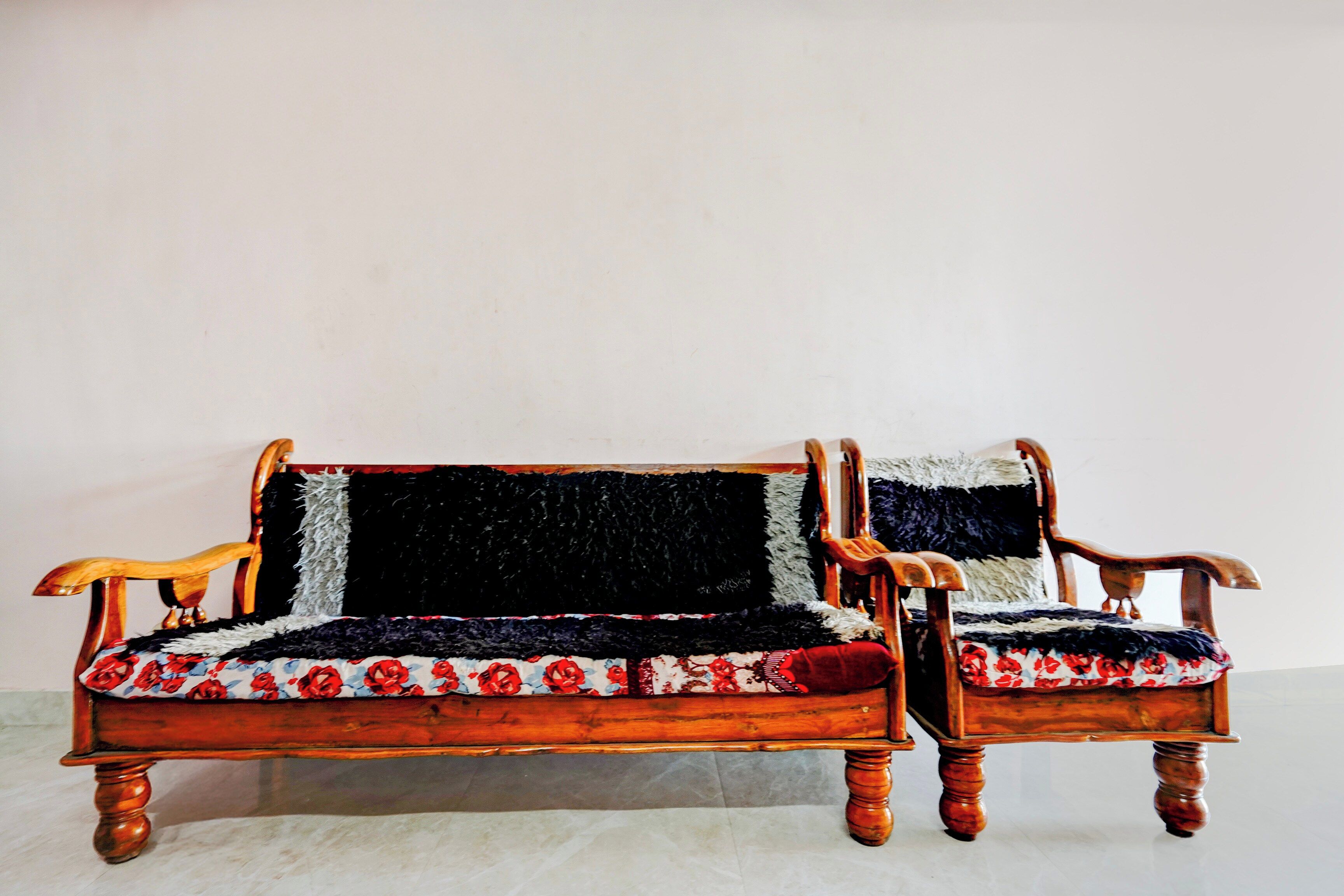 Ein Holzsofa mit einem floralen Kissen und ein passender Sessel, beide mit dunkel geprägter Rückenlehne.