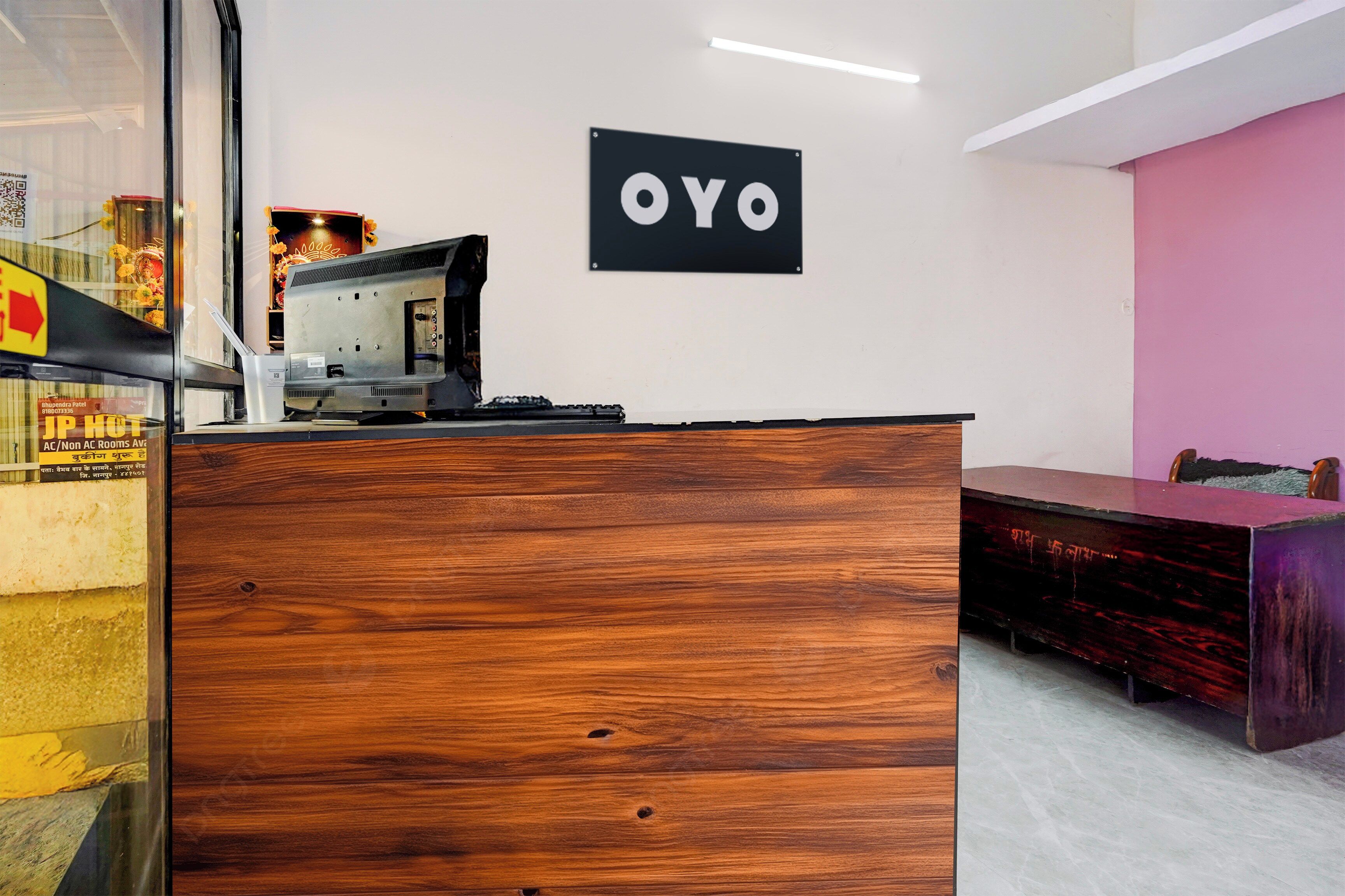 A reception desk with a wooden finish, a black sign with the word 'OYO' above it, and a pink wall in the background.