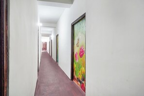 A long, narrow hallway with white walls and a red carpet. There are doors on both sides, and one door has a colorful painting of flowers and a butterfly.