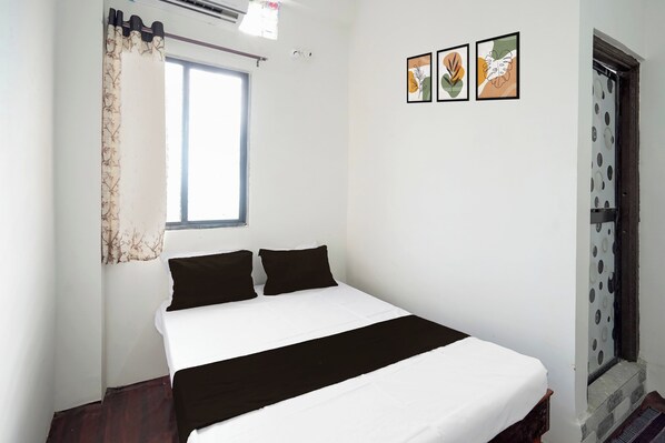 A bedroom with a bed, a window with curtains, and three wall-mounted pictures.