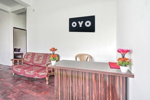 Un comptoir d’accueil avec une enseigne au-dessus, un canapé, deux fauteuils et deux vases de fleurs.