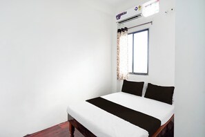 A bedroom with a bed, white walls, a window with curtains, and an air conditioning unit.