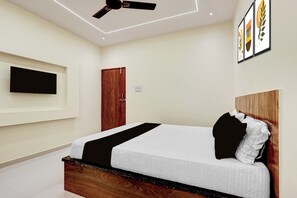 Quarto com cama, ventilador de teto, televisão fixada na parede e uma porta.