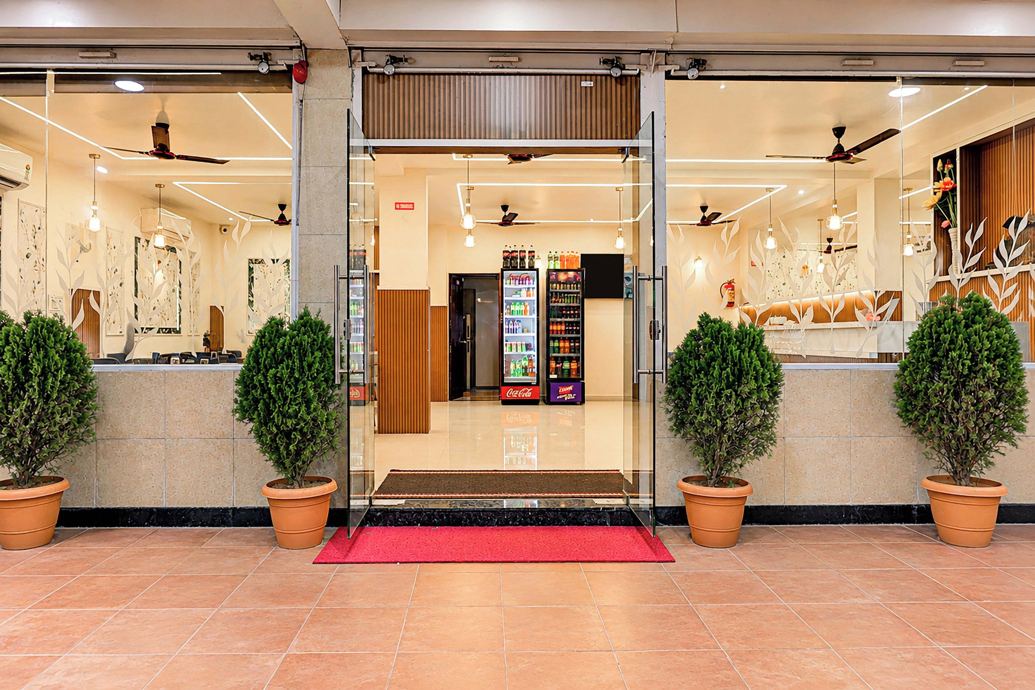 A hotel entrance with a red carpet, potted plants, and a vending machine.