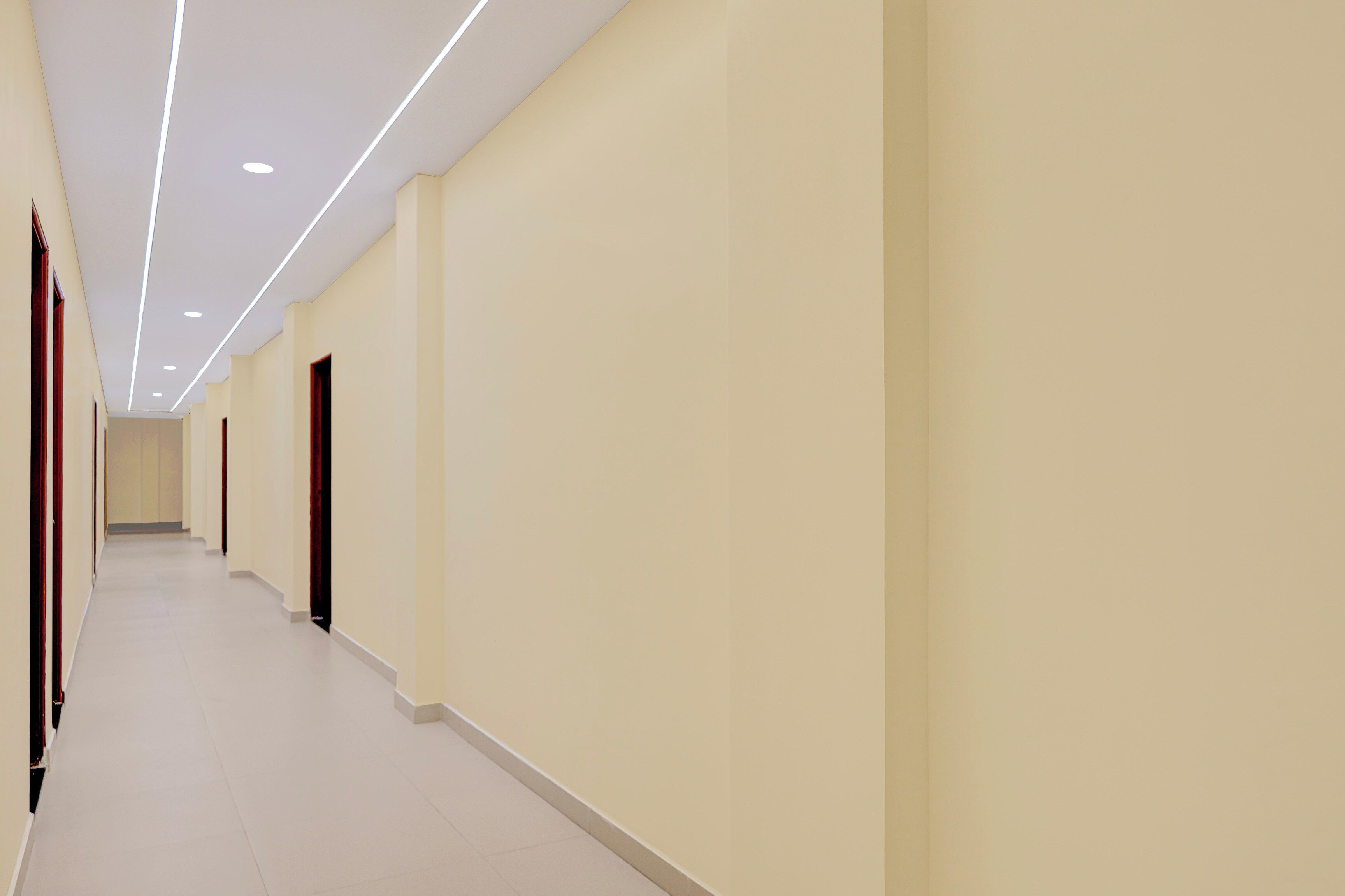 Un passadís llarg i estret amb una llum de sostre contínua, parets sense adorn i portes amb marc fosc.