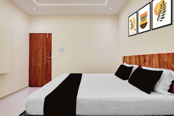 A hotel room with a wooden door, a bed with white and black bedding, and three framed artworks on the wall.