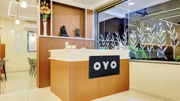 Balcão de recepção com placa indicando 'OYO', em ambiente moderno com painel de madeira e uma grande janela com folhagem decorativa.