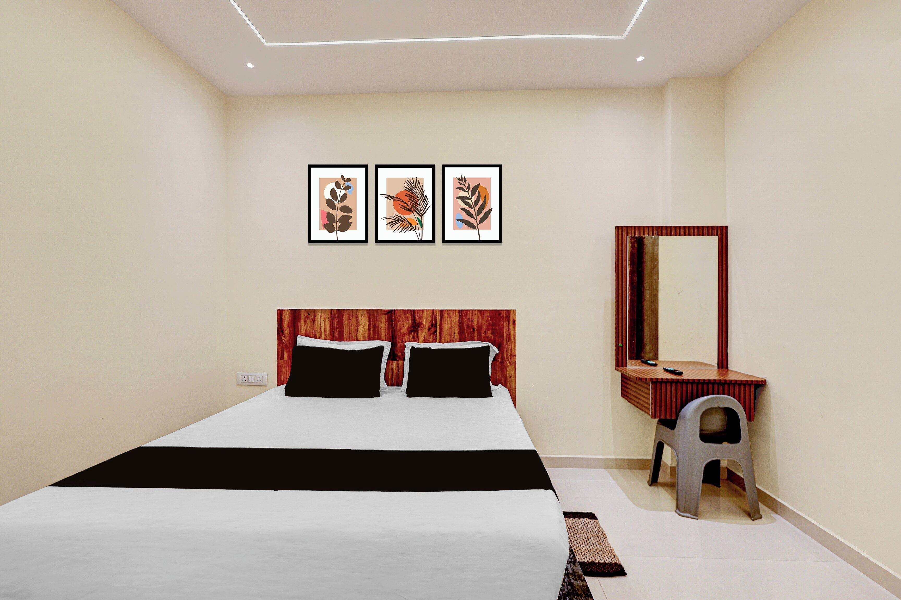 Une chambre à coucher comprenant un lit, une tête de lit en bois, une table de chevet, un miroir et trois œuvres d’art encadrées accrochées au mur.