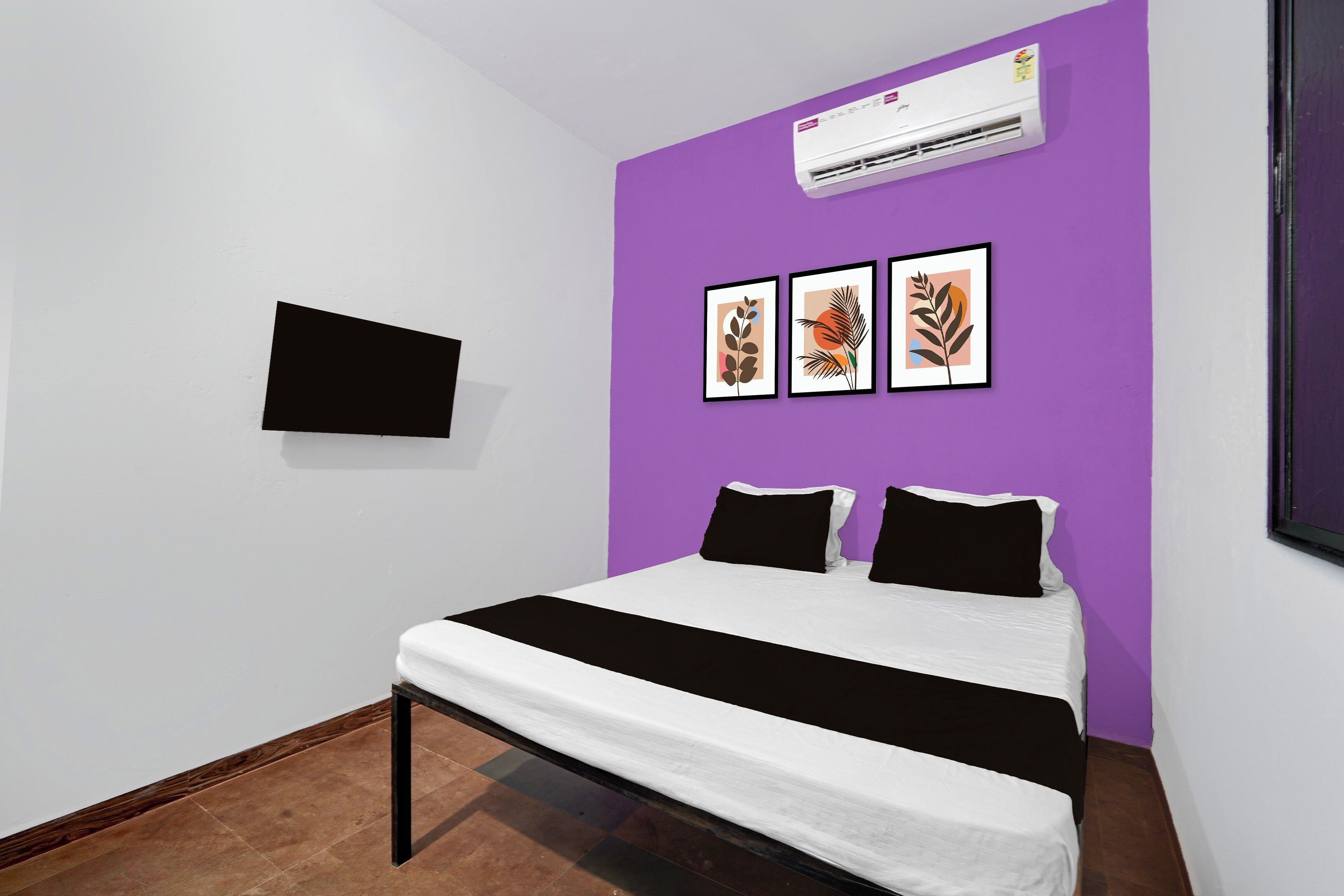 Un dormitorio con una cama, un televisor montado en la pared y tres cuadros enmarcados.
