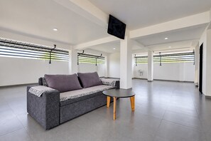 Un interior moderno con un sofá gris, una mesita redonda y un televisor de pantalla plana montado en el techo.