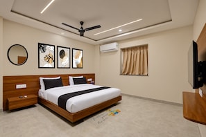 A hotel room with a bed, bedside tables, a ceiling fan, wall-mounted air conditioning, a window with curtains, and artwork on the wall. - Hotel O SN HOTEL (Nagpur)