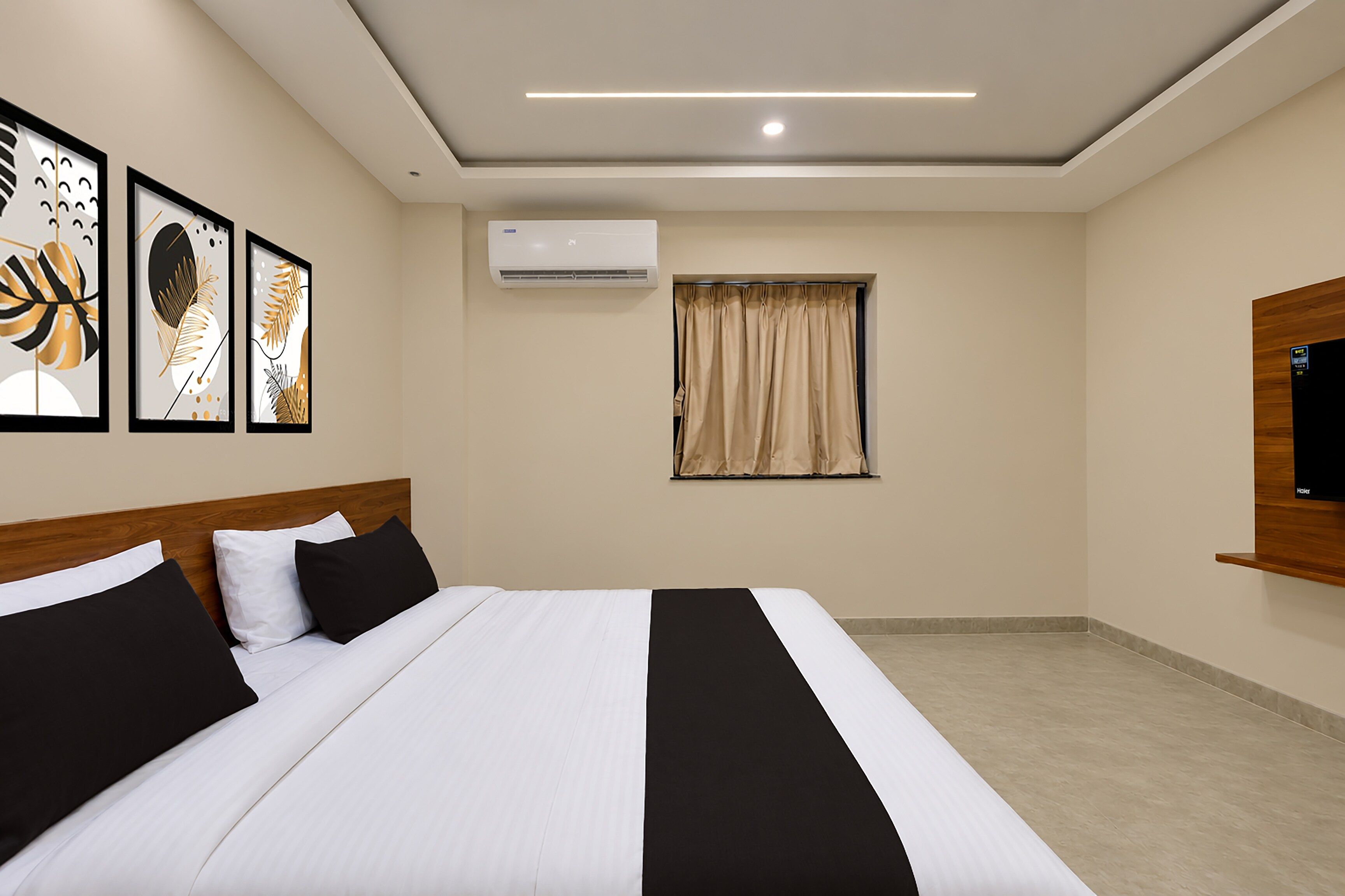 Quarto de hotel com cama, televisão de tela plana, ar condicionado, janela com cortinas e obras de arte na parede.