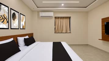 Quarto de hotel com cama, televisão de tela plana, ar condicionado, janela com cortinas e obras de arte na parede.