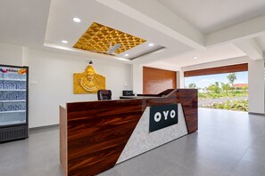 Un mostrador de recepción con acabado de madera y un cartel que dice 'OYO'. Encima del mostrador hay una obra de arte montada en la pared y una máquina expendedora a la izquierda.
