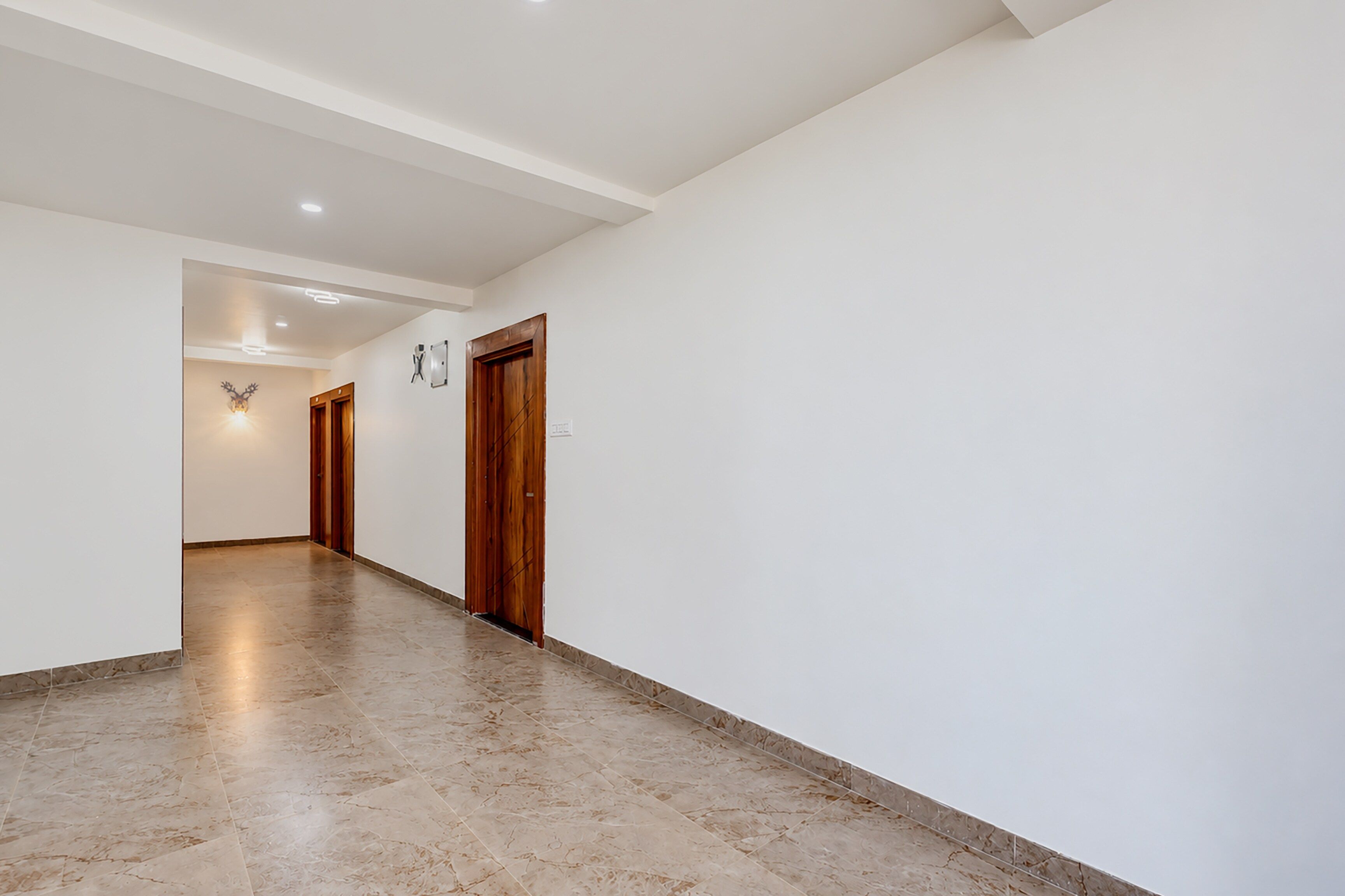 Un pasillo con piso de mármol, paredes blancas y puertas de madera.
