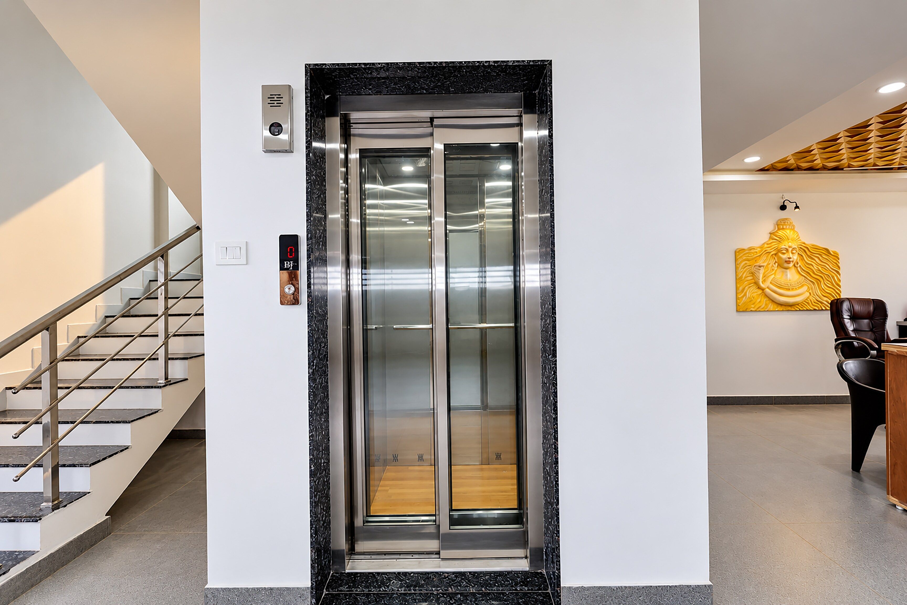 Um elevador moderno com visor digital, uma escadaria com grades de metal e uma obra de arte na parede.