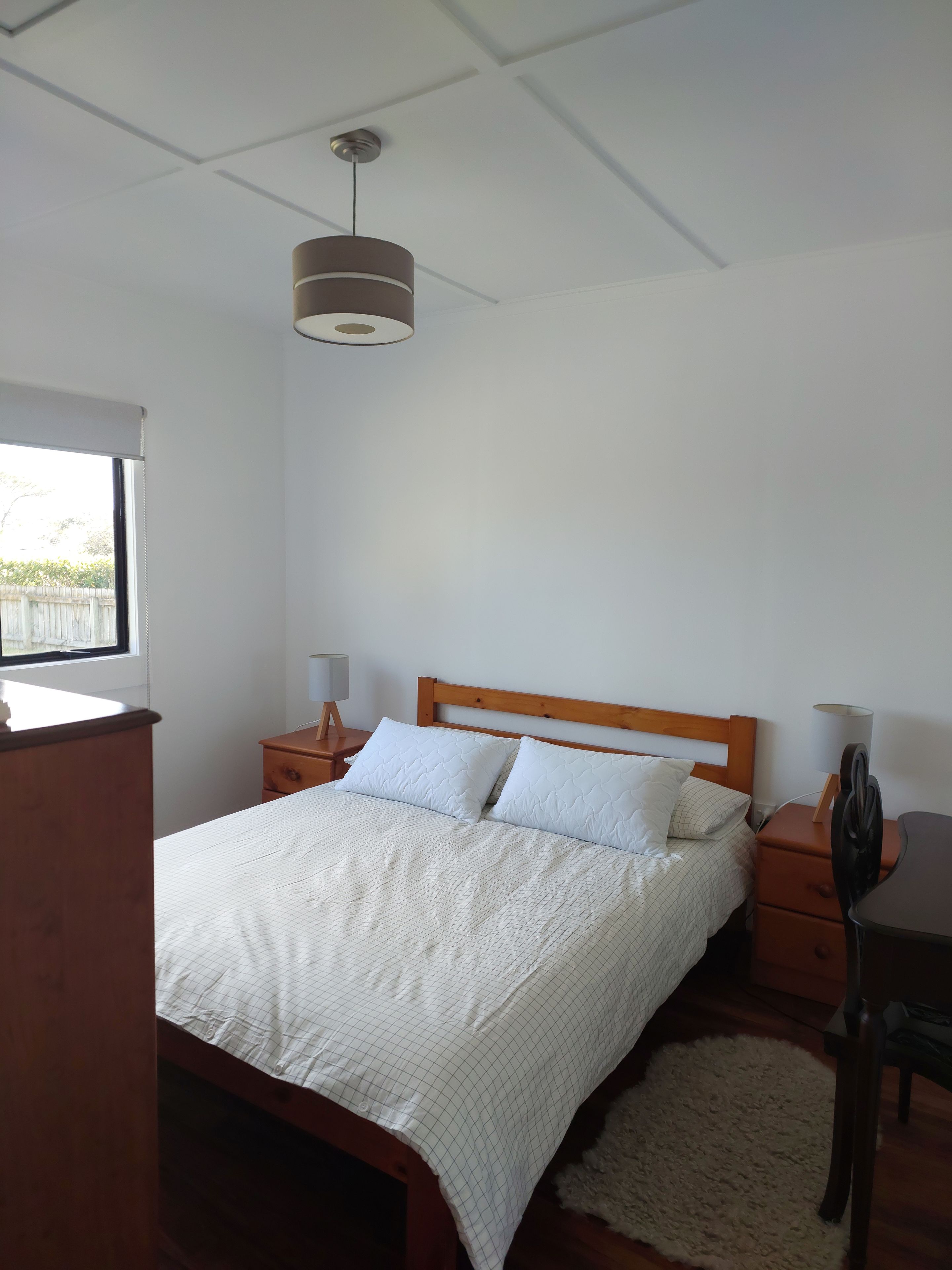 A bedroom with a bed, wooden headboard, bedside tables, a lamp, a desk, and a window.