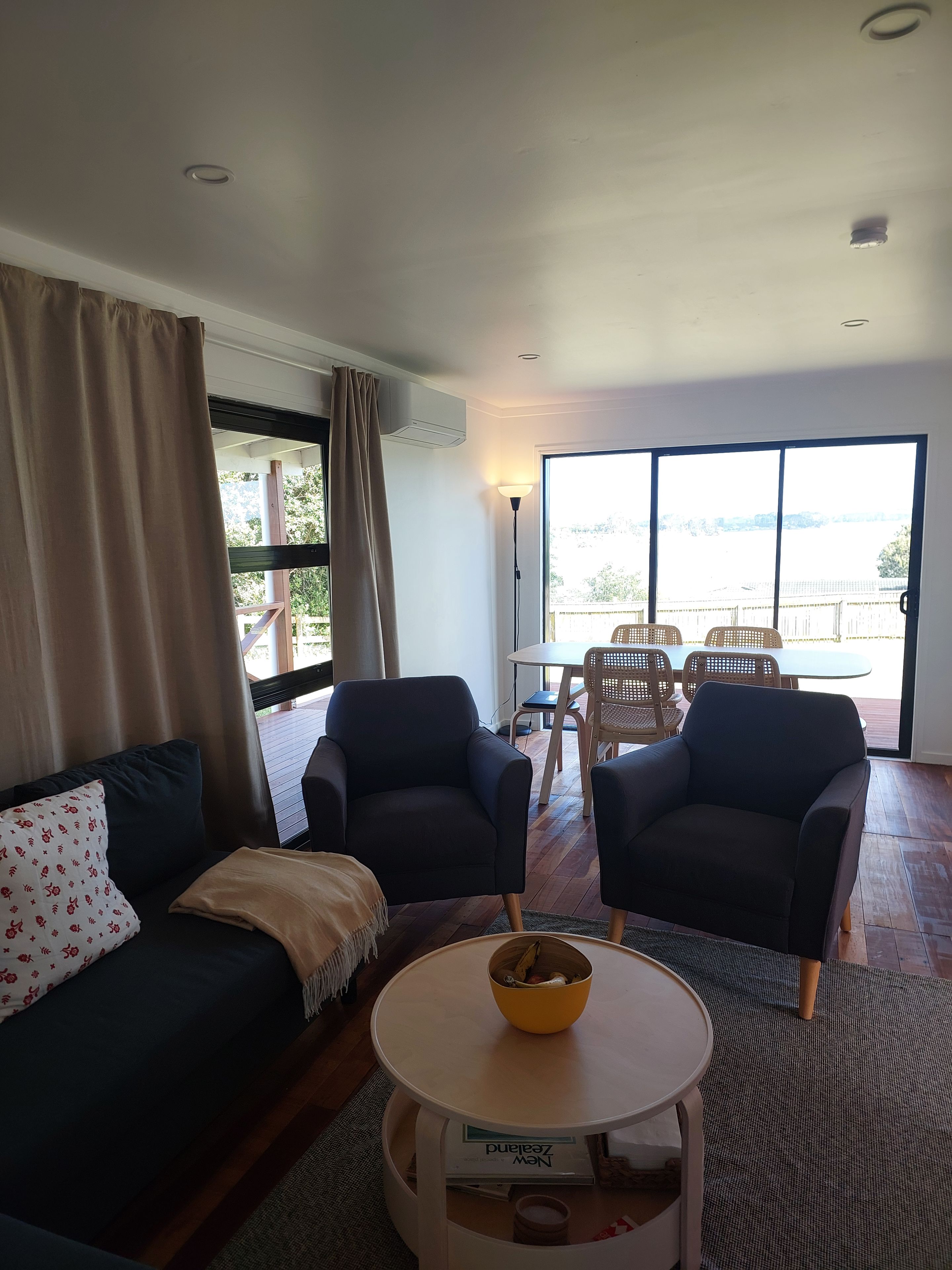 A living room with a sofa, two armchairs, a coffee table, and a view through large windows.