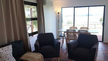 A living room with a sofa, two armchairs, a coffee table, and a view through large windows.
