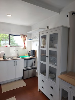 A kitchen with white cabinets, a microwave, a sink, and a cabinet with glass doors.