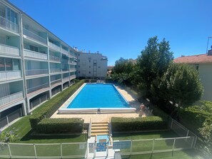 A swimming pool surrounded by a well-maintained lawn and a multi-story building with balconies. - New Listing (Canet-en-Roussillon)