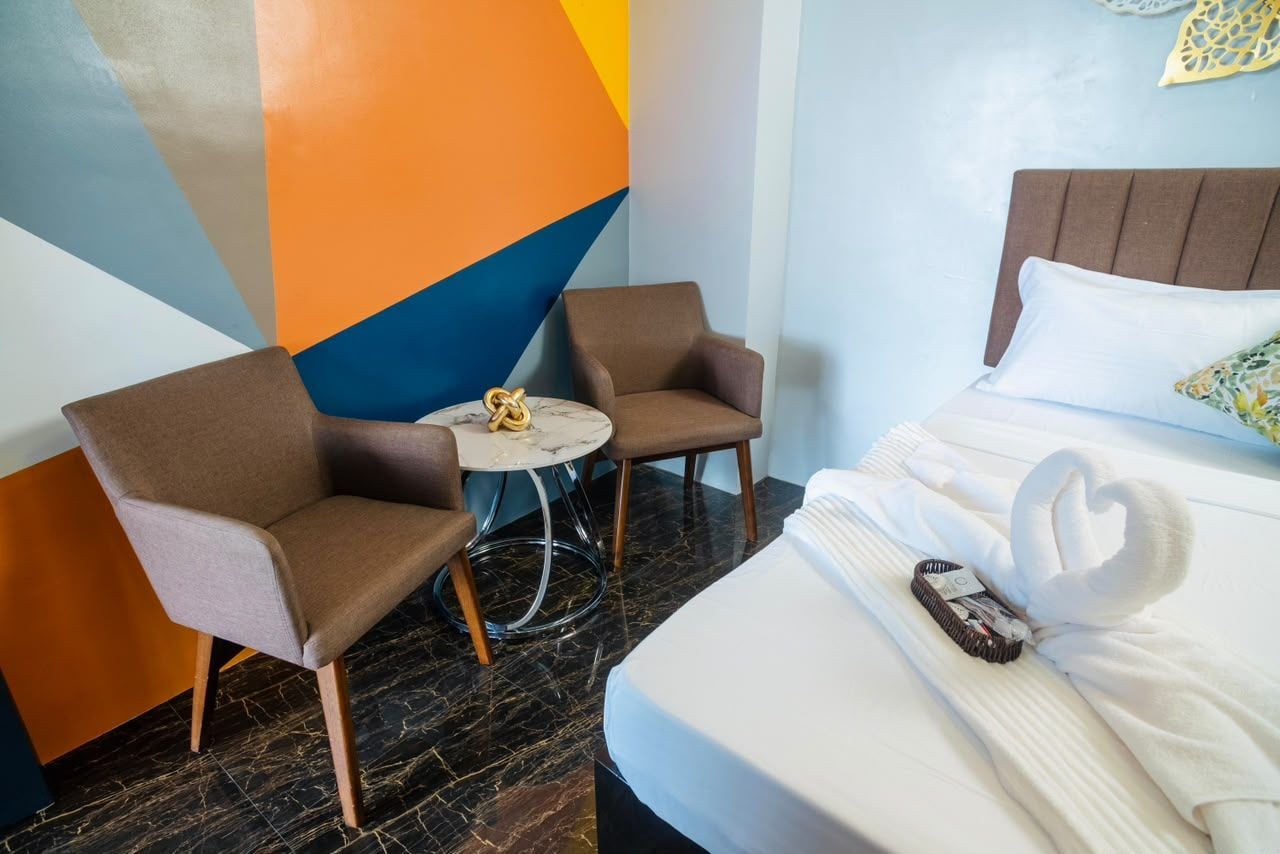 Ett hotellrum med en säng, två fåtöljer, ett litet runt bord och en dekorativ vägg.