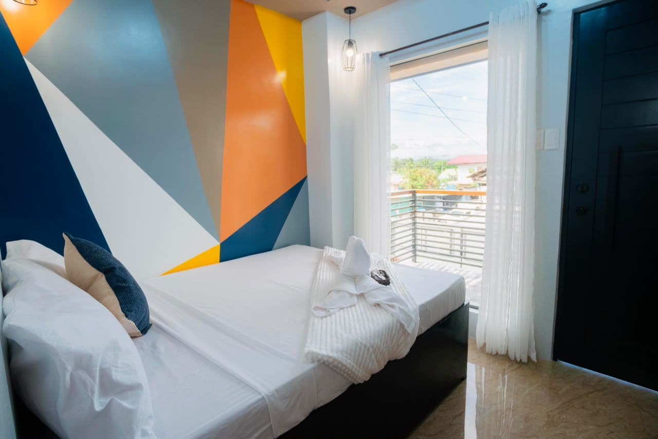 A hotel room with a bed, a window with curtains, and a view of the outside.