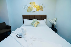 Una camera d'hotel con un letto, un cuscino, un comodino con un vaso di fiori e una decorazione a parete.