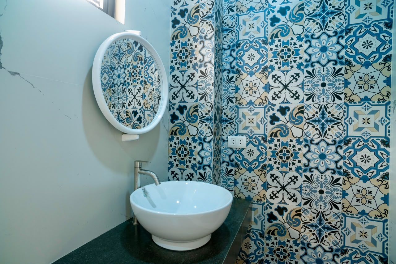 A bathroom with a white sink, a mirror, and patterned tiles.